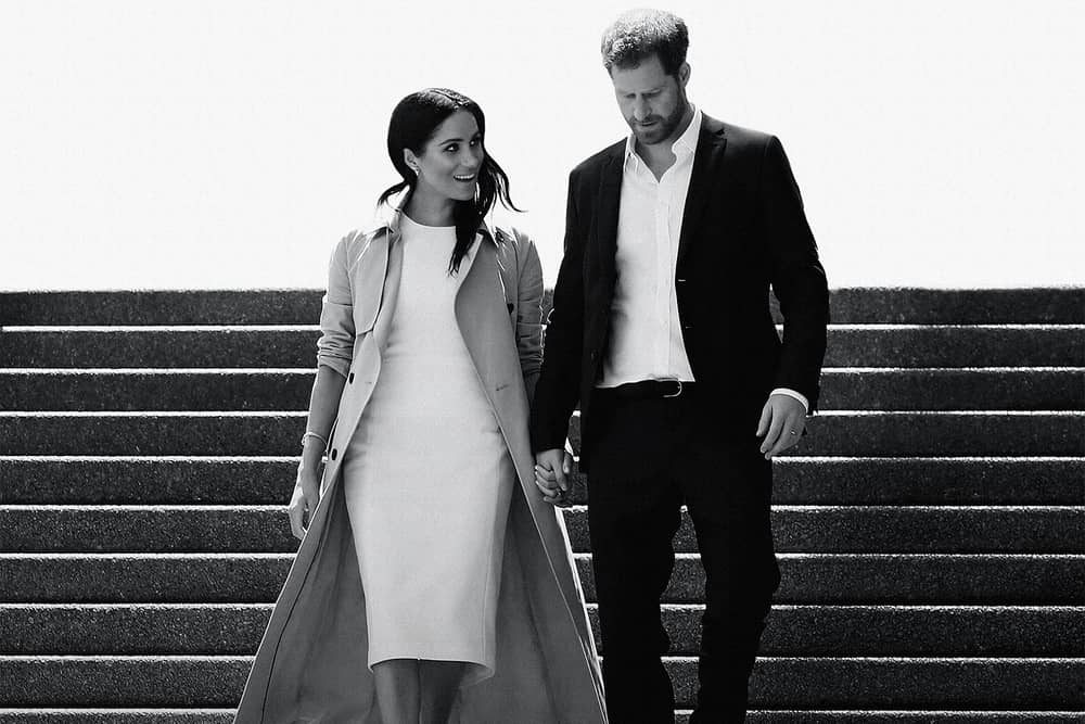 A black and white image of Meghan Markle and Prince Harry walking down a flight of stairs together, hand in hand and smiling (Credit: Netflix) 