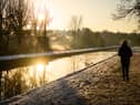 A man walks on the snow-covered path by the New River at sunrise, as steam rises from nearby houses in London.