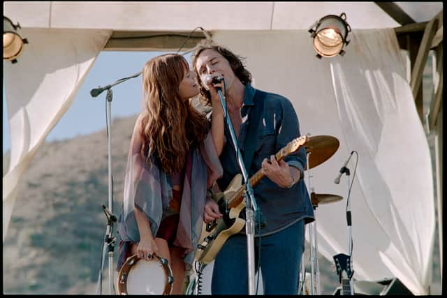 Riley Keough as Daisy Jones and Sam Claflin as Billy Dunne in Daisy Jones & The Six, singing into a shared microphone (Credit: Lacey Terrell/Prime Video)