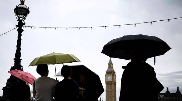 Pedestrian stand under umbrellas while looking at Elizabeth Tower, commonly called Big Ben from the Southbank by the River Thames, in central London, on July 31, 2023 on a gloomy and rainy summer day.