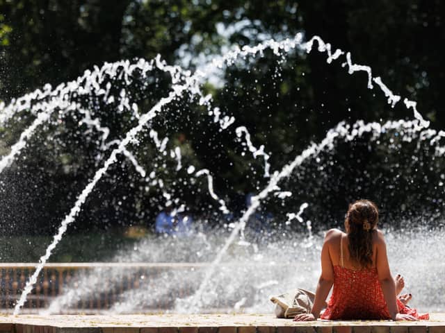 A woman sits by fountains in warm weather.