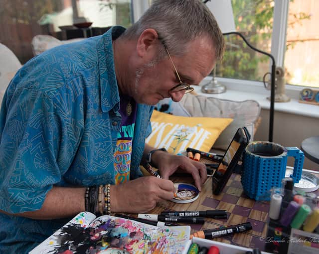Mark Taylor painting one of his recycled jam jar lids, which he gives out at music shows and events.