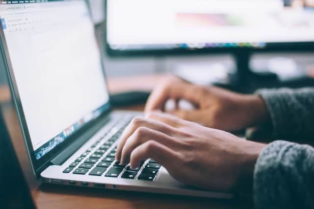 A person types on a laptop keyboard while working at a desk with a computer monitor in the background.