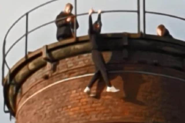 The braindead youth hangs from the top of the chimney by one arm as his mates look on