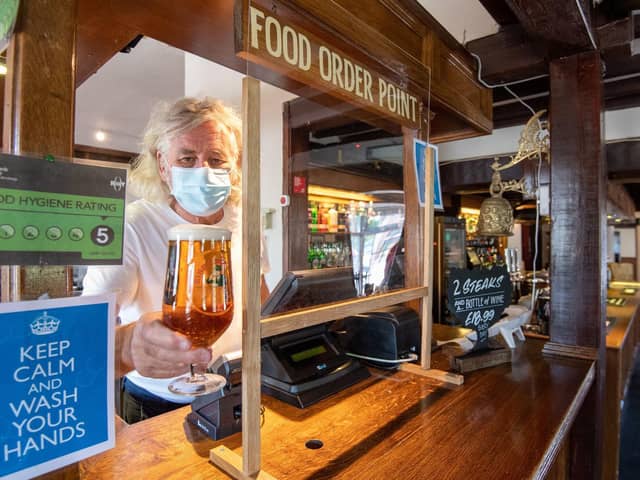 A publican presents a pint from behind a protective screen. Picture by PA.