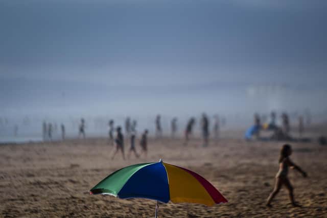 An umbrella stands on the sand as beachgoers enjoy a day at Costa da Caparica beach in Almada