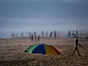 An umbrella stands on the sand as beachgoers enjoy a day at Costa da Caparica beach in Almada