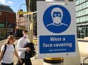 Pedestrians walk past a sign urging people to 'wear a face covering' due to the COVID-19 pandemic, in Manchester (Photo by OLI SCARFF/AFP via Getty Images)