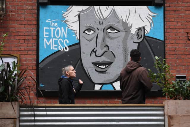 People walk past a mural depicting Britain's Prime Minister Boris Johnson on the front of a closed pub in Manchester