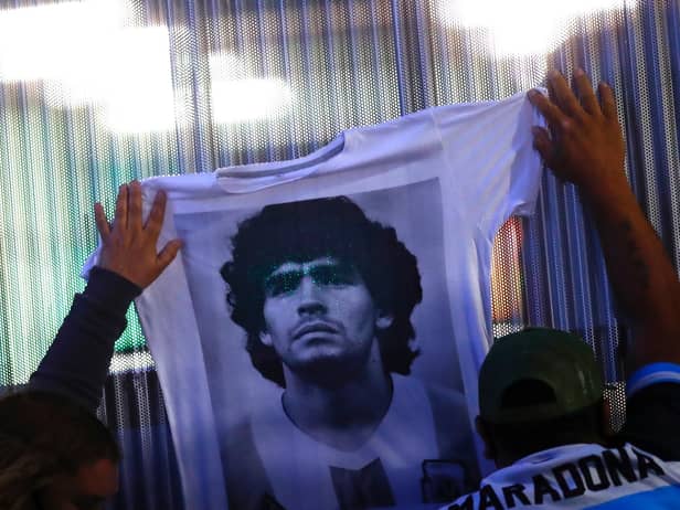 Fans hold a jersey with the face of Diego Maradona at Clínica Olivos on November 03, 2020 in Olivos, Argentina. Personal doctor of Maradona, Leopoldo Luque, confirmed the former footballer was to undergo surgery to treat a clot in his brain