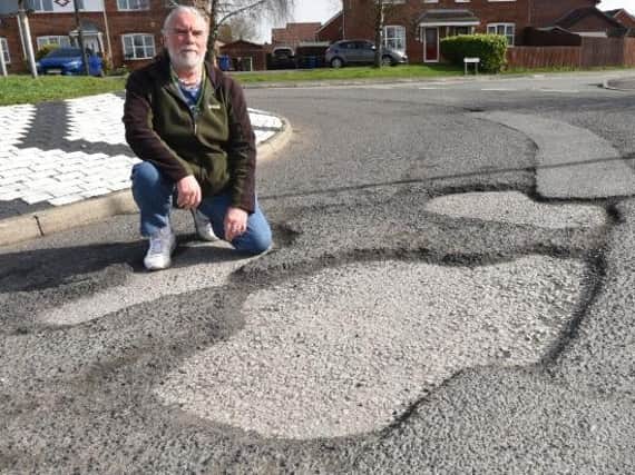 Coun John Vickers examines one of the potholes in his community