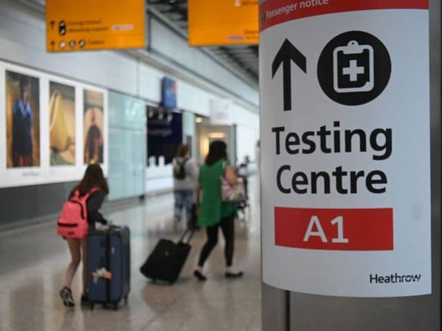 Passengers push their luggage past signage displaying the way to a Covid-19 test centre, in Terminal 5 at Heathrow airport