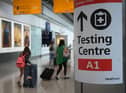 Passengers push their luggage past signage displaying the way to a Covid-19 test centre, in Terminal 5 at Heathrow airport