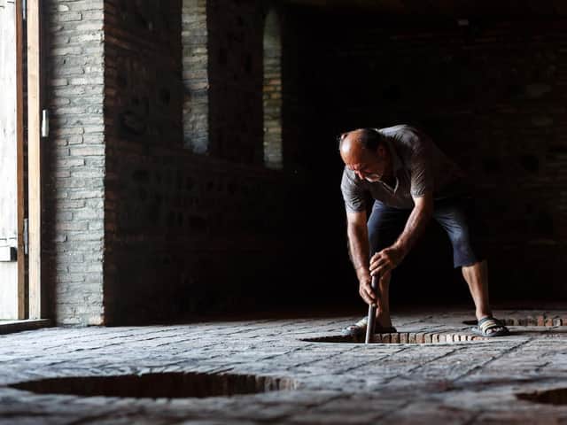 A winemaker looks over his red wine, fermenting in a qvervi buried in the soil of a winery. Picture: Miles WIllis