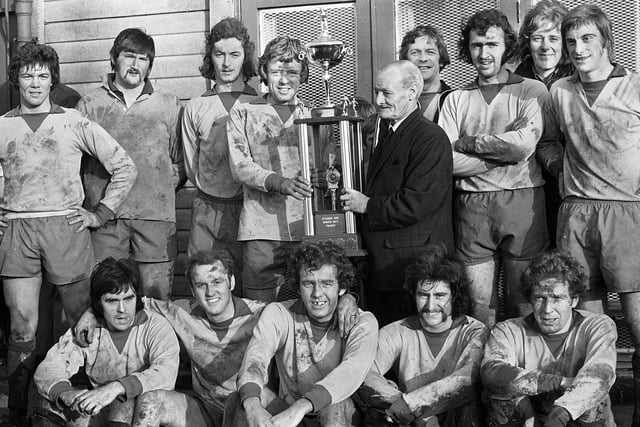 Standish captain, Harry Archer, receives the Hurst Trophy from Jimmy Hurst, President of the Post and Chronicle Sunday Soccer League, surrounded by team-mates. Standish had beaten Beech Hill 2-1 after extra time in the final at Ashton Town's ground on Sunday 22nd of December 1974.