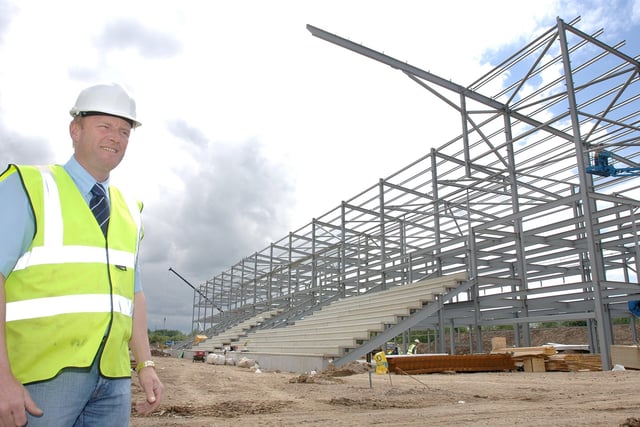 The main stand of the new Leigh Sports Village Stadium begins to take shape behind site manager Bill Anderson, of Hall Construction. May  2007.