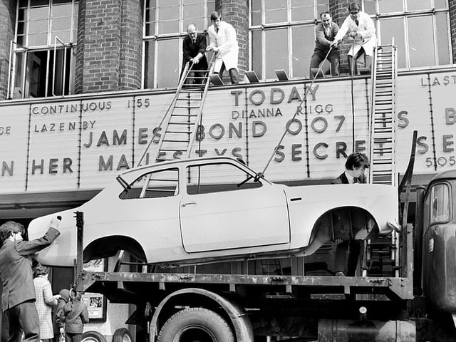 A Ford Escort car is hauled onto the roof section of the entrance to the ABC cinema in Station Road to publicise the latest James Bond film "On Her Majestys Secret Service" in 1970. Cinema manager, Derek Fuller, is on the roof, right.