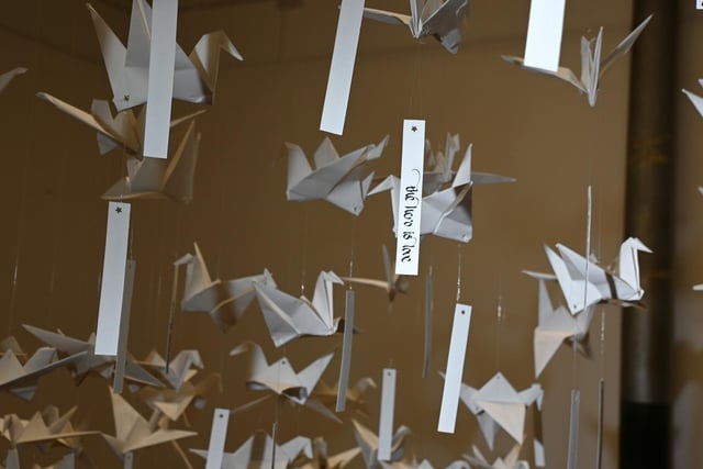 1,000 origami paper cranes, each with haiku poetry attached, hung from the ceiling to create a murmuration of handmade birds in flight.