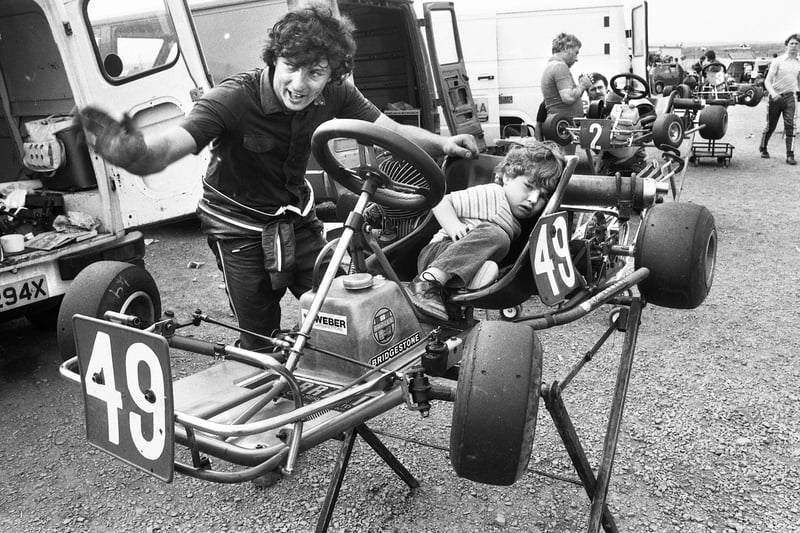 Wigan racer Andrew Fairless prepares his kart as his two-year-old daughter Dawn snuggles up at the Champions of Three Sisters National Kart Races on Sunday 24th of July 1983.