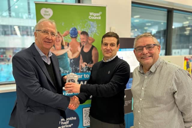 Leader of Wigan Council, Coun David Molyneux MBE (left) and Coun Chris Ready (right) present a Fitbit Sense 2 health tracker to Be Well member Christian Worthington - winner of Be Well's recent Thanks A Million prize draw celebrating more than a million visits to Be Well leisure centres in 2022.