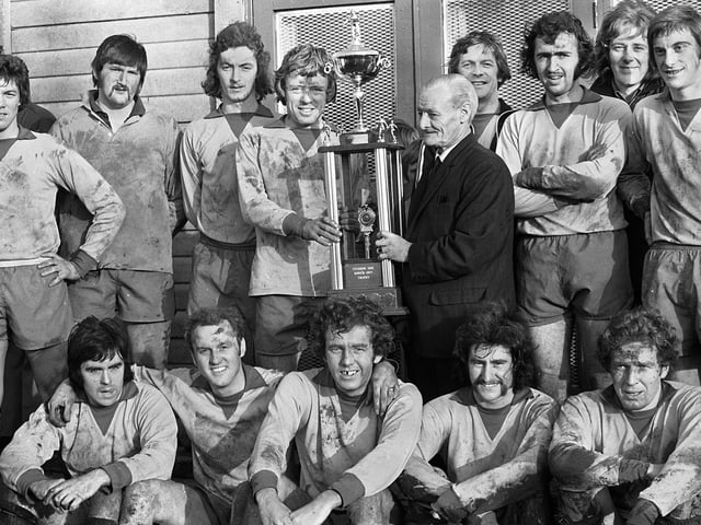 Standish captain, Harry Archer, receives the Hurst Trophy from Jimmy Hurst, President of the Post and Chronicle Sunday Soccer League, surrounded by team-mates. Standish had beaten Beech Hill 2-1 after extra time in the final at Ashton Town's ground on Sunday 22nd of December 1974.