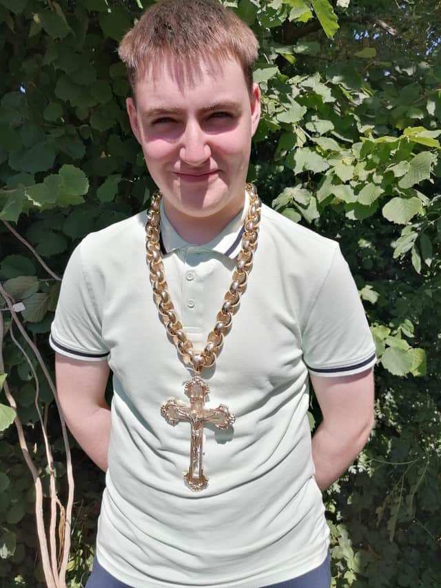 Hansons Auctioneers' trainee valuer Daniel Armstrong wears the chain. See SWNS story SWMRcross; The biggest gold crucifix and chain in the UK which weighs 1.5kg is set to fetch £30k at auction - with bling-loving boxers Tyson Fury and Anthony Joshua being offered first dibs.