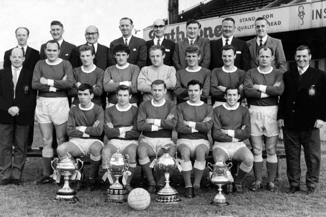 The Wigan Athletic team and officials in the highly successful 1966-67 season.
Players, back row, left to right, Derek Houghton, Dave Roberts, Stuart Houghton, Alan Halsall, Dennis Crompton, Roy Wilkinson, Alfie Craig.
Front row, l to r, John Ryan, Bert Llewellyn, Harry Lyon, Allan Brown, Walter Stanley.
The trophies are, left to right, Edward Case Cup, Cheshire League Cup, Lancashire Junior Cup and Liverpool Senior Non League Cup.   