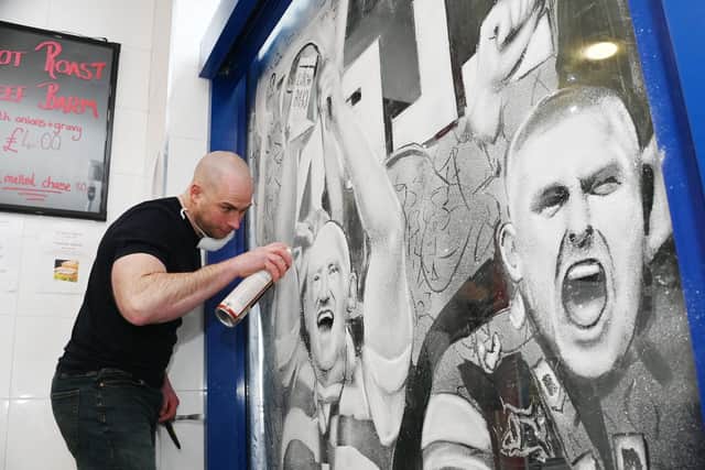 Scott Wilcock, artist known as Snow Graffiti, at work on a mural celebrating Wigan Warriors World Club Challenge victory, on the window of A Fine Kettle of Fish