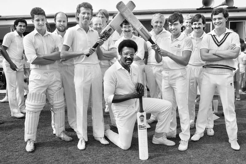West Indian and Lancashire cricket legend Clive Lloyd under the bats held by Warren Aspinall, right, Everton and ex Wigan Athletic striker, and Gordon Bennett, captain for the day, before Lloyd's testimonial match at Orrell Red Triangle Cricket Club on Sunday 29th of June 1986.