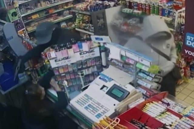 A masked gunman leans over the counter as one of the staff members cowers