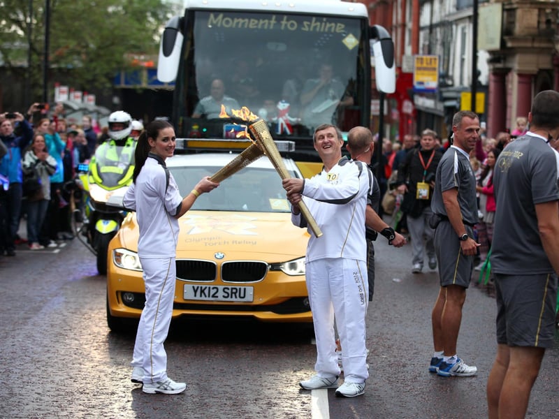 Torchbearer 100 Kirsty Gallacher passes the Olympic Flame to Torchbearer 101 Norman Brown on the Torch Relay leg between Wigan and Ince-in-Makerfield.
