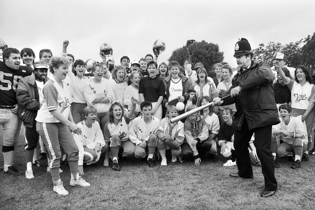 Bobby on the ball.....Area Constable Jim Bolton swops his truncheon for a baseball bat with the encouragement of American softball teams and Wigan Wolverines American football team during a fun day at Goose Green on Saturday 8th of August 1987 in aid of the Children's Wheelchair Fund and Wigan Hospice. 