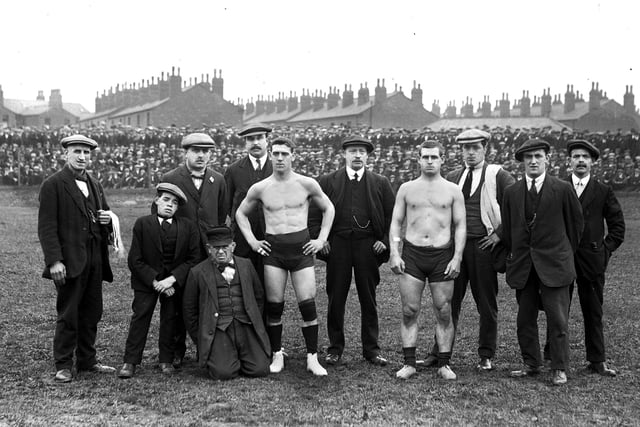 An outdoor wrestling bout in Wigan in the early part of the 20th century with the competitors and their handlers. 
The venue is probably Springfield Park where bouts were held in front of huge crowds well into the 1930s.
