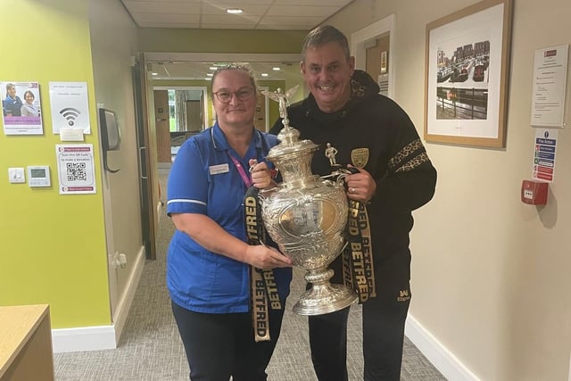 A staff member at Wigan and Leigh Hospice is shown the Challenge Cup trophy by Leigh Leopards' boss Derek Beaumont