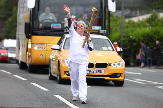 Torchbearer 098 Patricia Payne carries the Olympic Flame on the Torch Relay leg between Wigan and Ince-in-Makerfield.