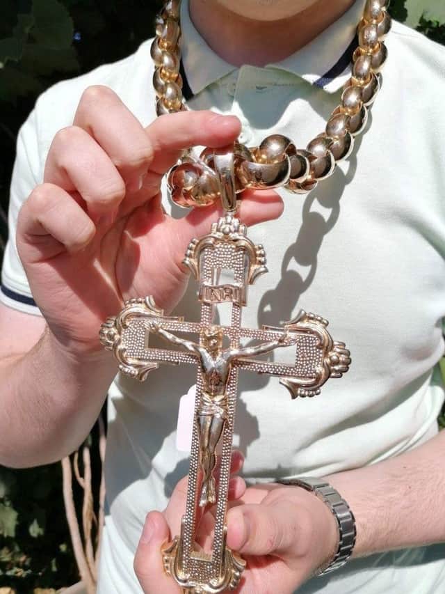 Hansons Auctioneers' trainee valuer Daniel Armstrong wears the chain. See SWNS story SWMRcross; The biggest gold crucifix and chain in the UK which weighs 1.5kg is set to fetch £30k at auction - with bling-loving boxers Tyson Fury and Anthony Joshua being offered first dibs.