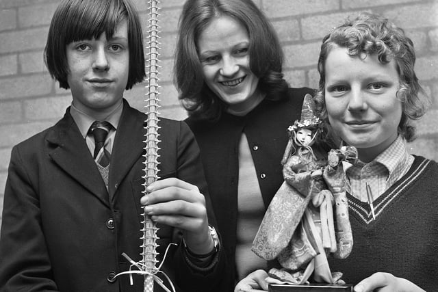 Teacher Miss C.W. Brown with pupils Ian Keegan and Gillian Howarth holding a shark's tooth sword stick from the New Zealand island of Nauru and doll from Taiwan during a Geography lesson in March 1972 at Hindley County Secondary School.