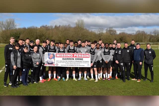 Wigan Athletic players and staff unfurl a banner appealing for help in finding devoted fan Darren Orme