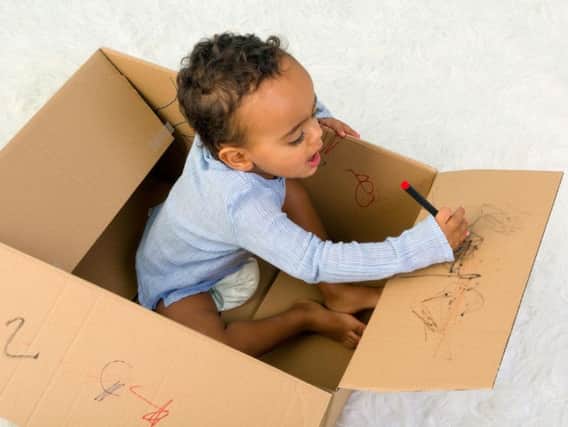 A child playing in a cardboard box with crayons