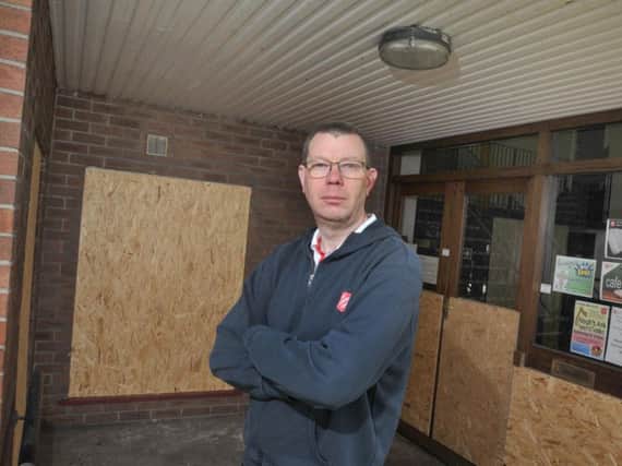 Corps officer Mark Lewis alongside the boarded-up windows which were smashed by the thieves
