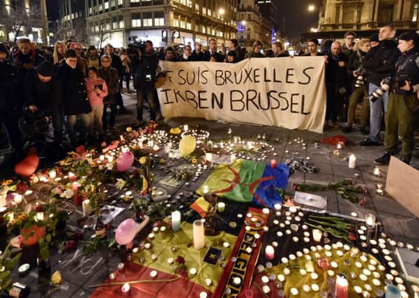 People holding a banner reading "I am Brussels" behind flowers and candles to mourn for the victims at Place de la Bourse in the center of Brussels