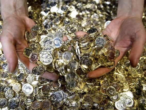 A worker grabs a handful of new 12-sided one pound coins from a metal crate as they are minted at the Royal Mint in Llantrisant, Wales