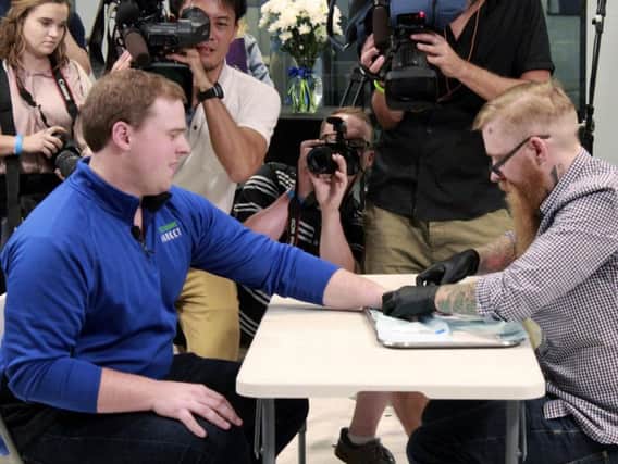 Tony Danna, left, vice president of international development at Three Square Market in River Falls, Wis., reacts while getting a microchip implanted in his left hand