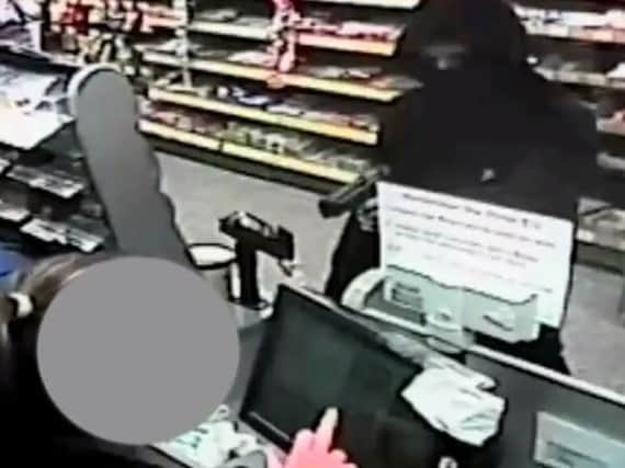 The robber points a handgun at a shop worker